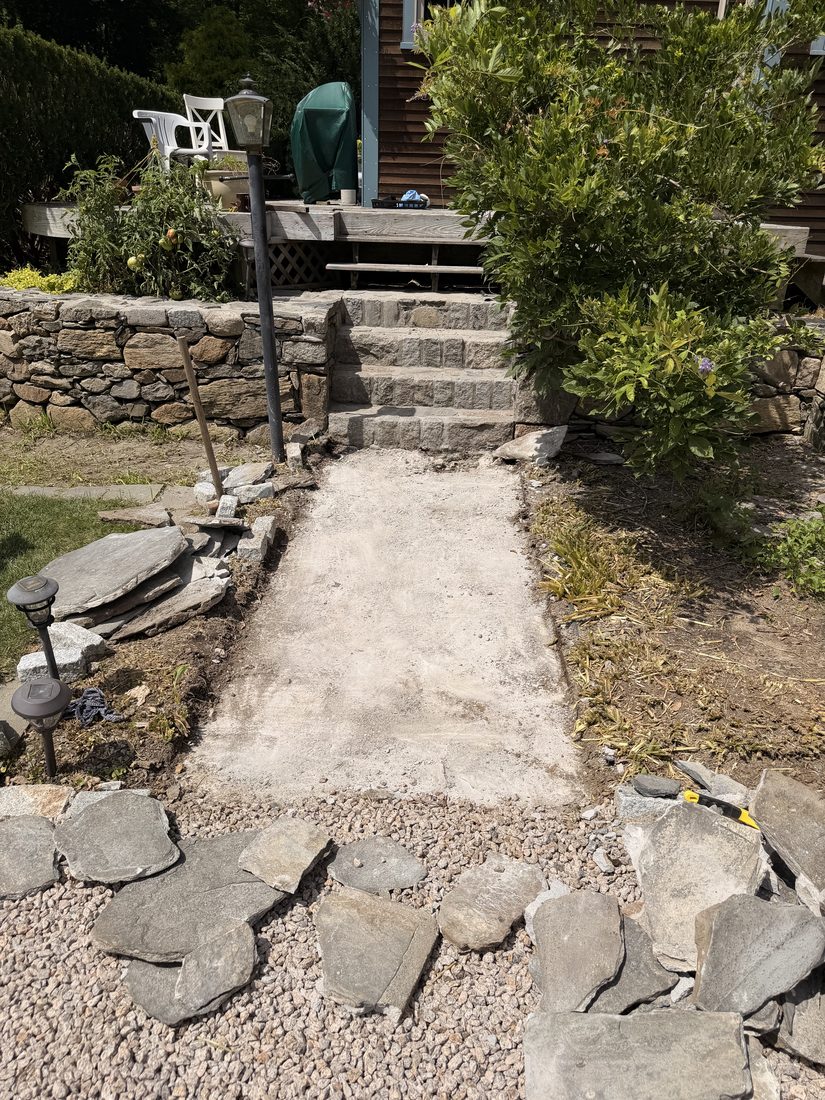 A poured concrete base cured and ready, with flagstone staged around it on the driveway
