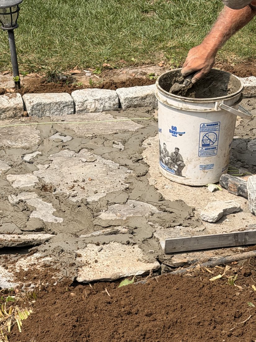 Mortar being buttered onto the concrete base before a flagstone is bedded
