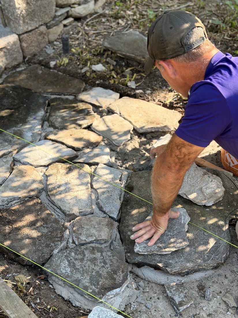 A mason setting a flagstone to a stringline pulled across the walk