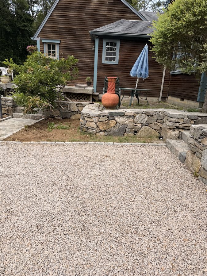 The terrace wall and steps seen across the driveway, the same view as the before frame