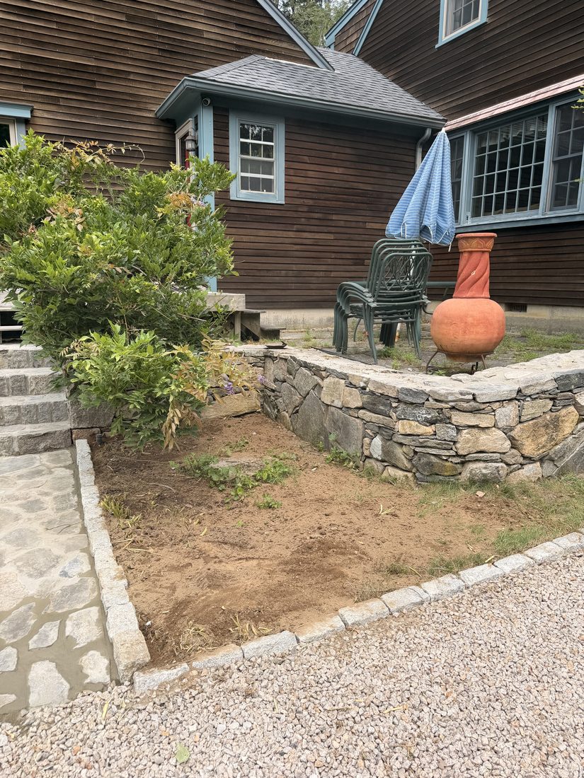 The fieldstone wall wrapping the deck terrace, with the ground regraded to meet it