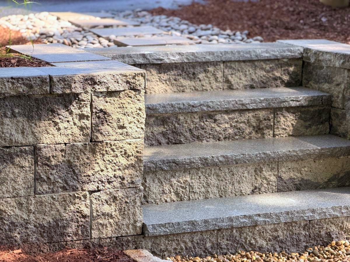 Finished granite steps turning off the block wall, with the walk running beyond