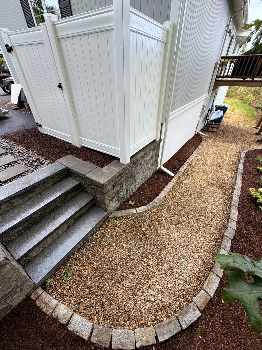 Granite steps and stacked stone skirt, with the cobble edge sweeping the washed stone around them in a single curve